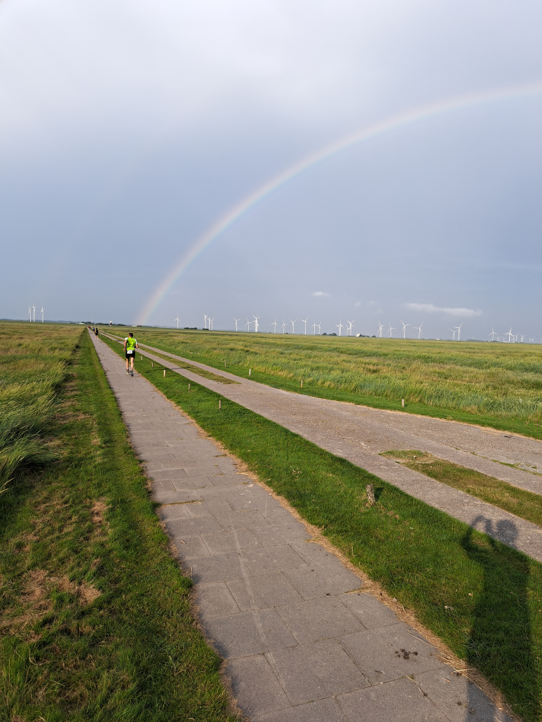 Läufer auf dem Rückweg beim Hallig Dreeathlon 2025, im Hintergrund Regenbogen und Windkraftanlagen